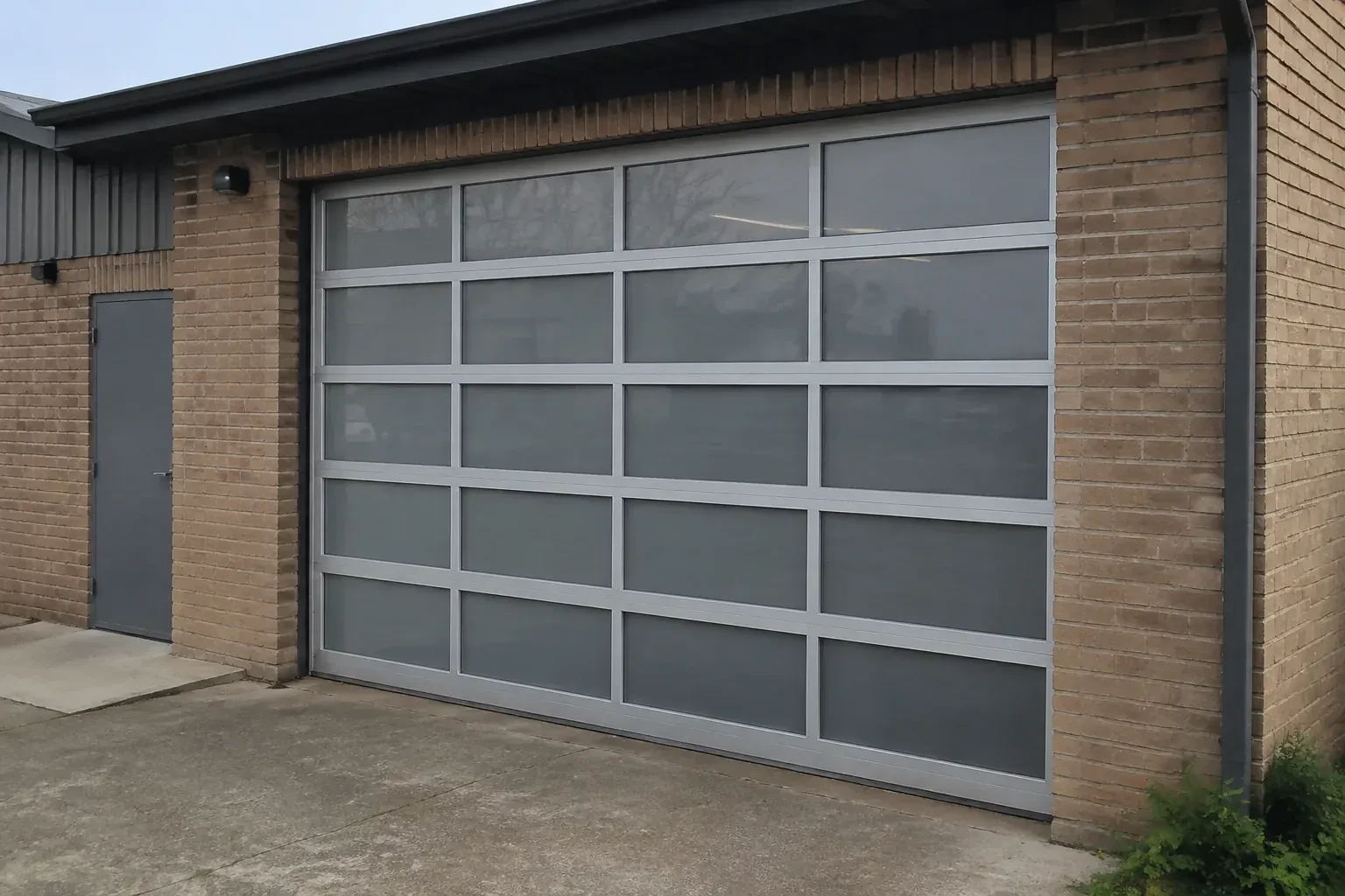 Closed glazed sectional door in a grey metal frame at a brick workshop. — Full-View Glass Garage Door Installation, Vaughan