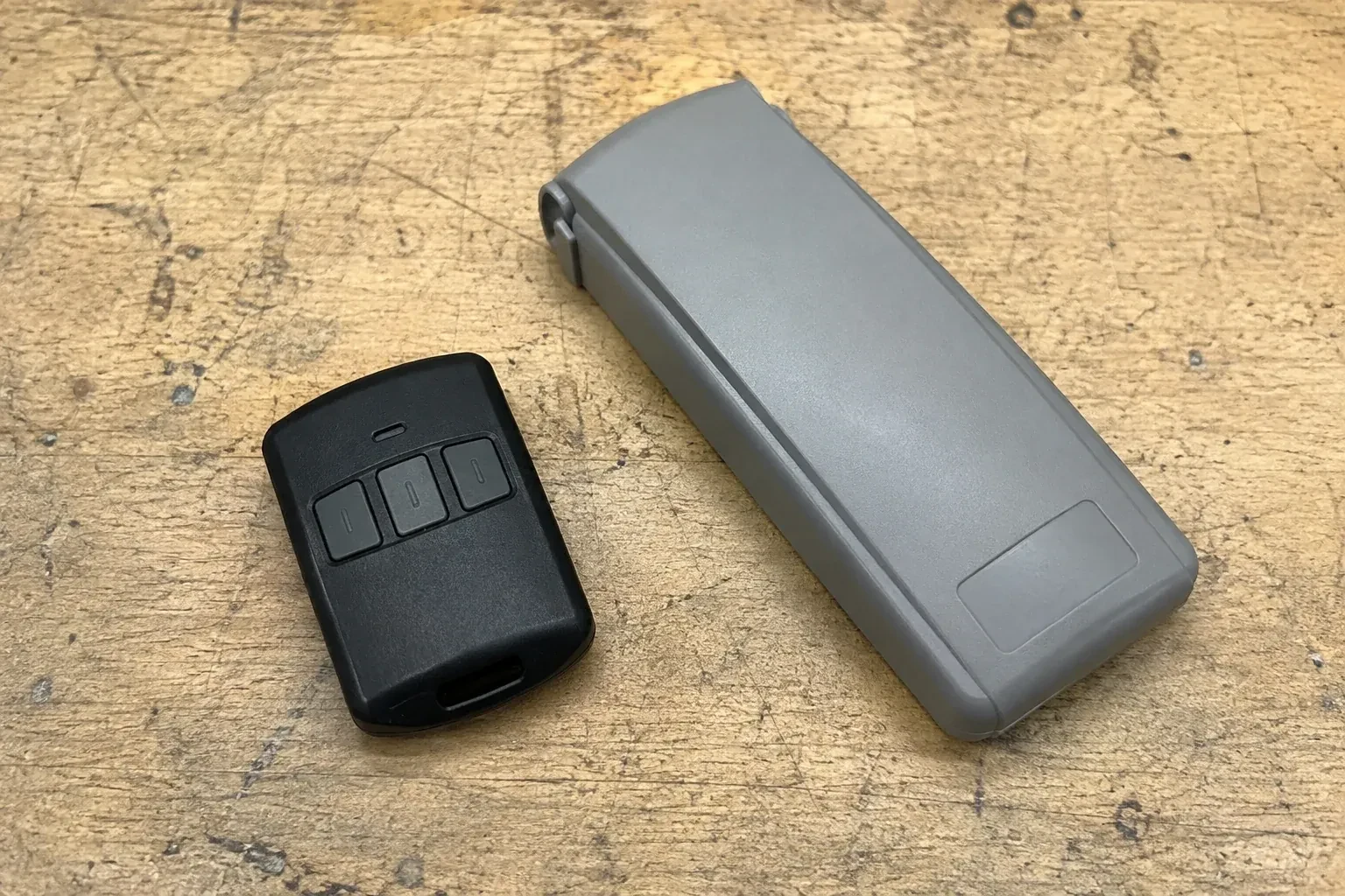 Three-button remote beside a closed grey keypad cover on a workbench. — Garage Door Remote and Keypad Programming, Vaughan