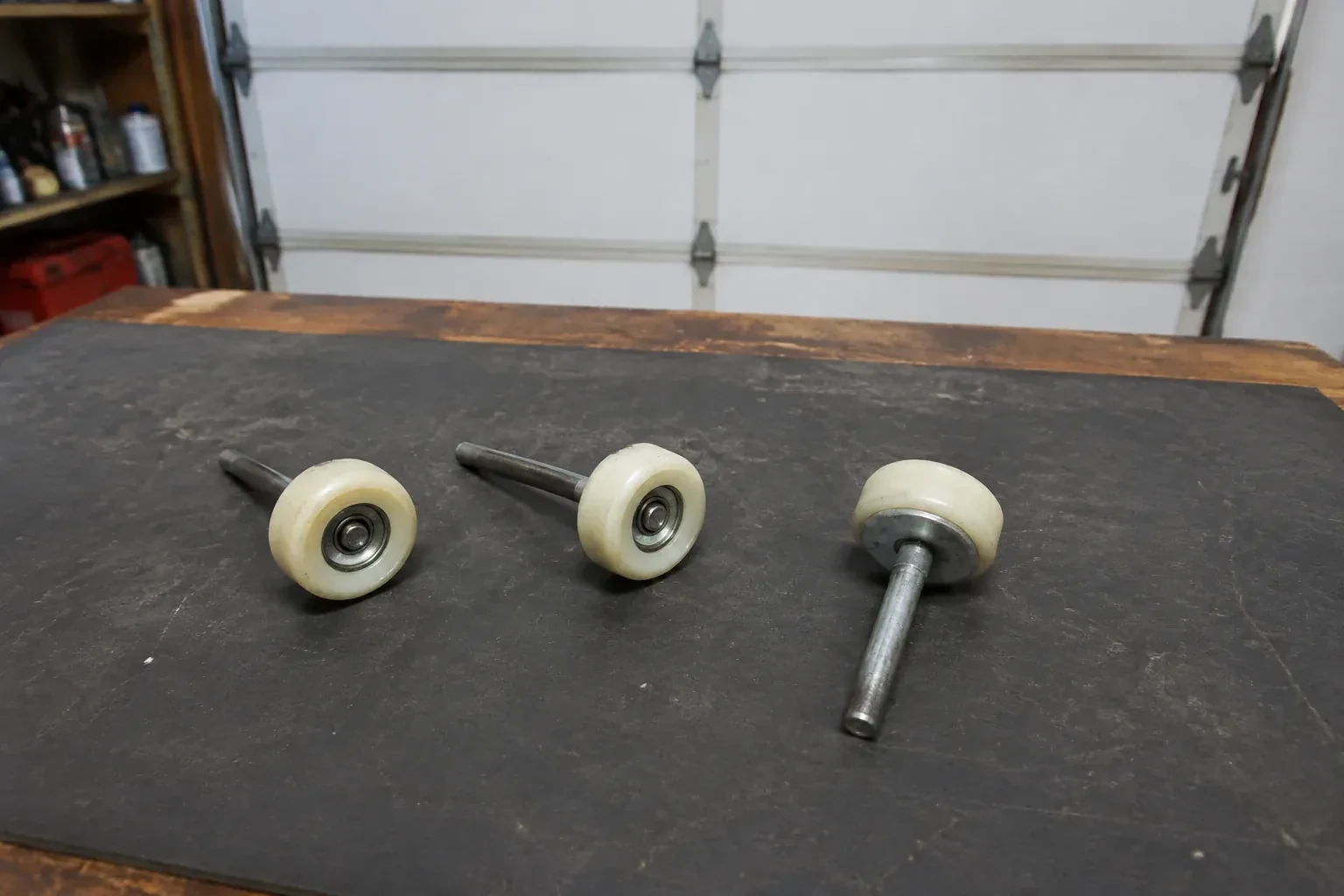 Three detached nylon-wheel garage door rollers with steel stems on a work mat. — Garage Door Roller Replacement, Vaughan