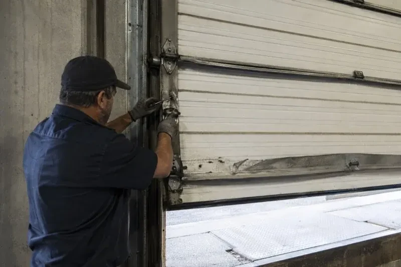 Person holding tools at the side hinge of a partly raised industrial sectional door — Commercial Sectional Door Repair, Vaughan