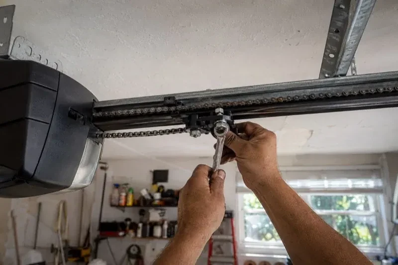 Hands holding a wrench against an opener trolley beneath a chain rail — Chain-Drive Opener Repair, Vaughan